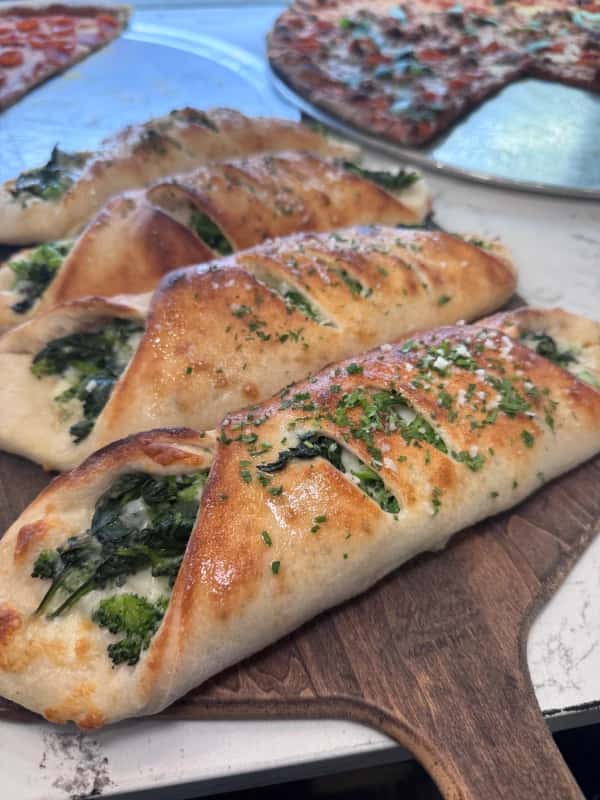 Freshly baked calzones filled with spinach and cheese, served at Crustinos Pizza in Rockaway Beach, highlighting their commitment to authentic, high-quality ingredients and traditional recipes.